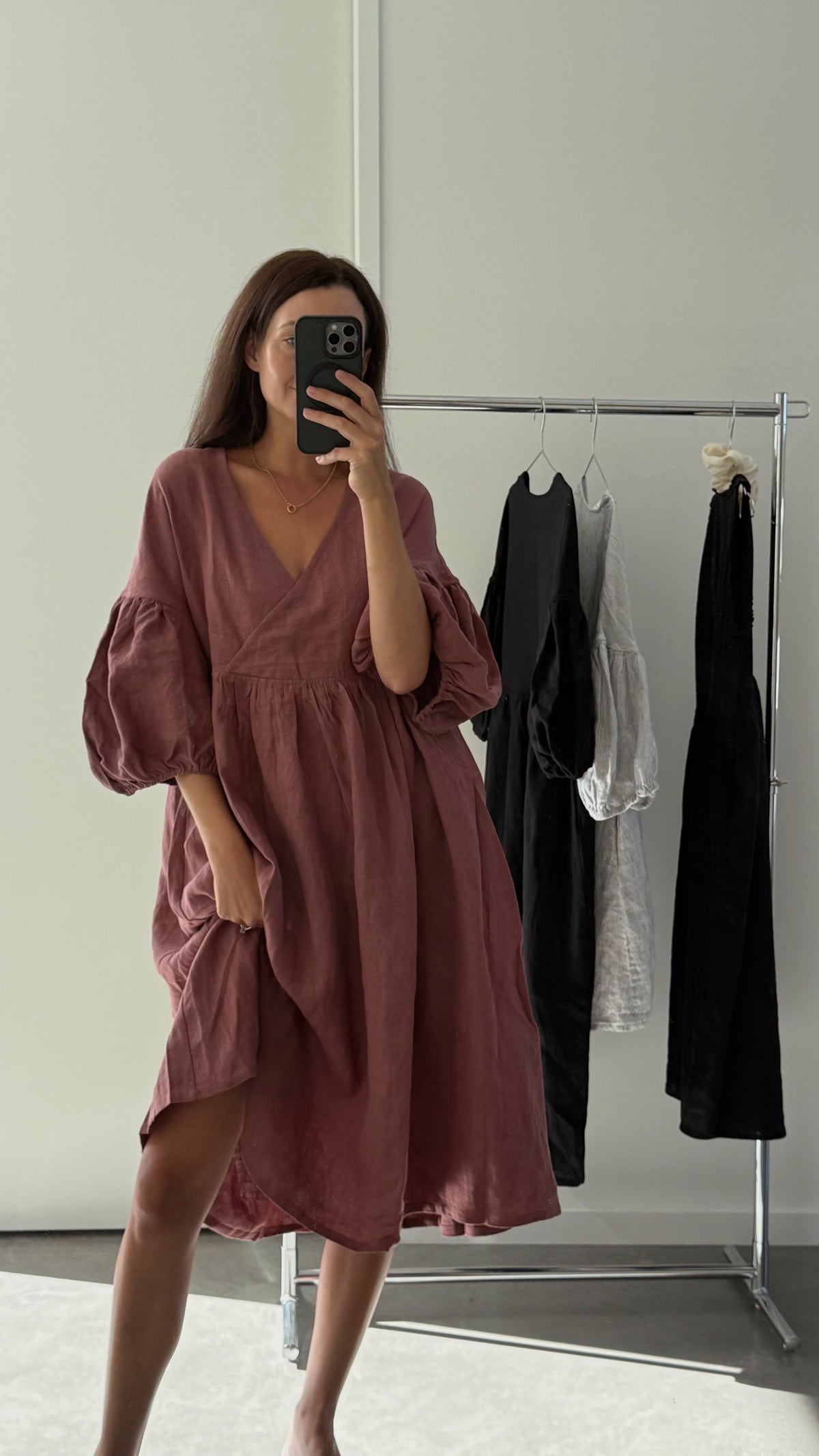 Woman wearing a rust-colored dress taking a mirror selfie in a minimalistic room.