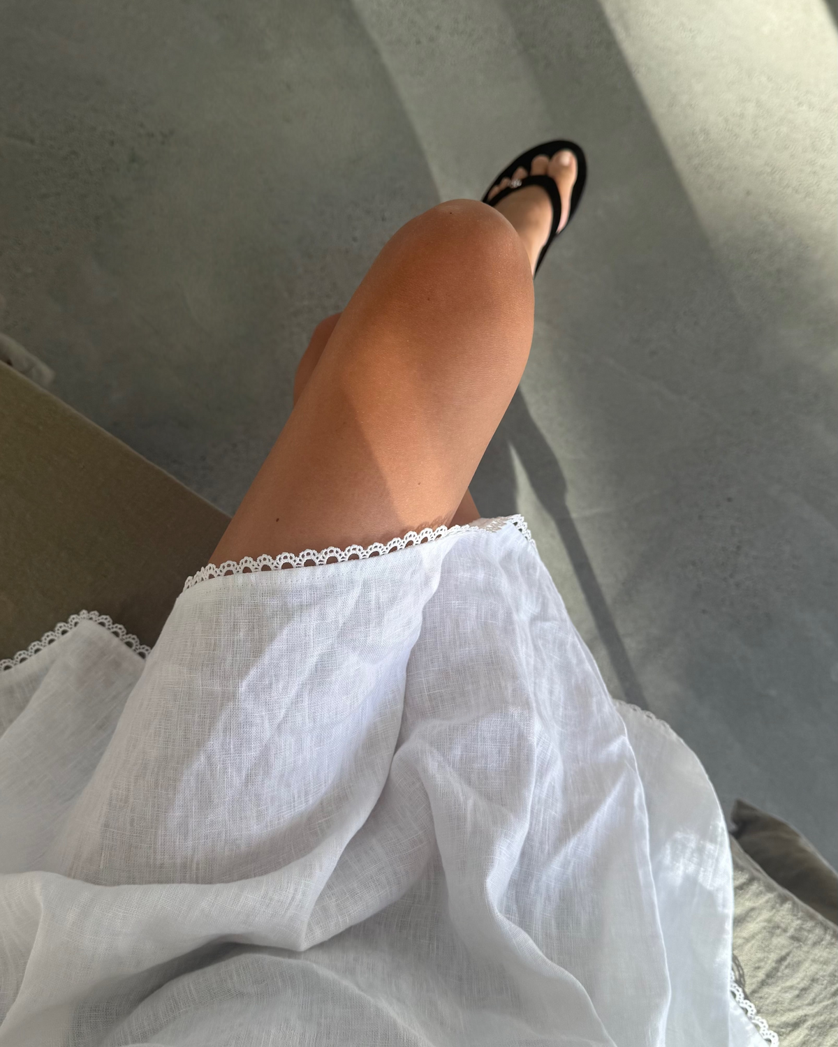 Person wearing a white skirt and black sandals on a gray floor.